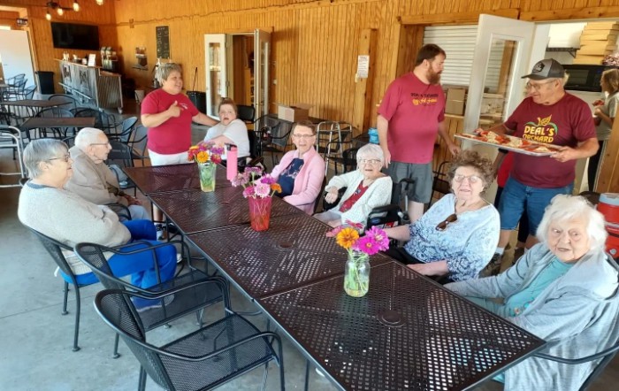 A group of people sitting around a table with flowers, enjoying a social gathering outdoors.