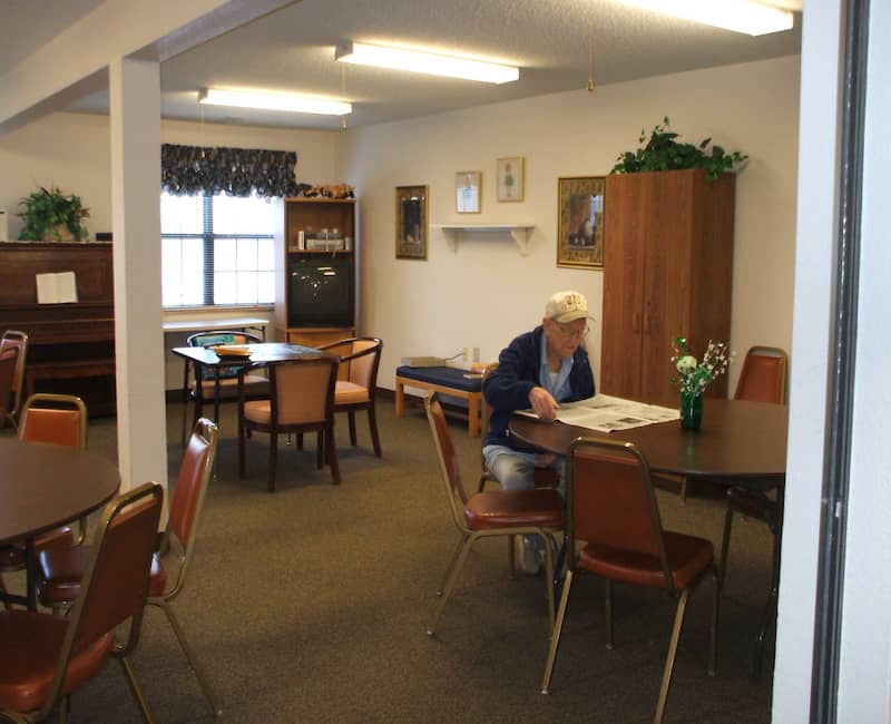 A senior person reading at a table in a quiet community center room.