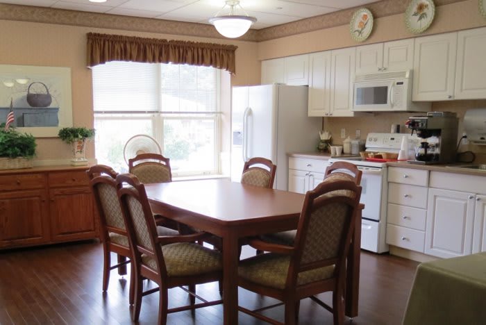 A cozy kitchen and dining area with a wooden table and chairs, white appliances, and large windows.