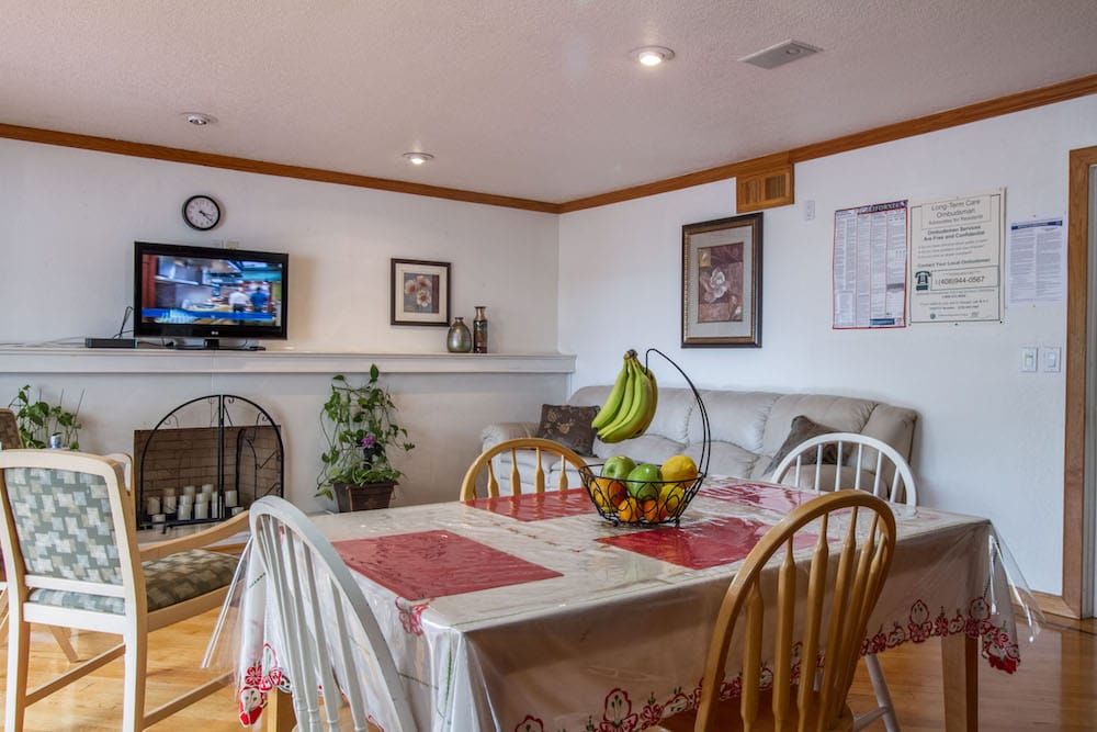 A cozy dining area with a table set for meals, featuring a fruit bowl centerpiece and a TV in the background.