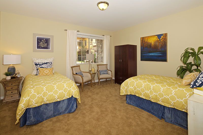 A cozy bedroom featuring twin beds with yellow bedding, two chairs, and decorative artwork on the walls.