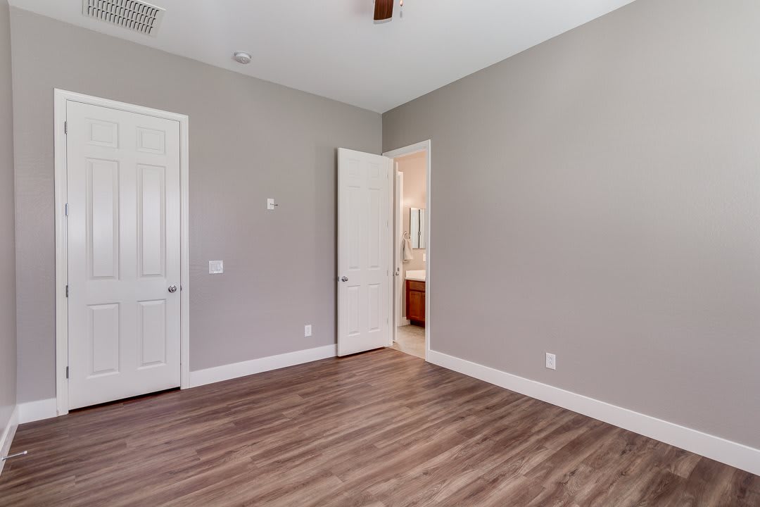A vacant room featuring wood flooring and neutral-colored walls, with a view into an adjoining bathroom.