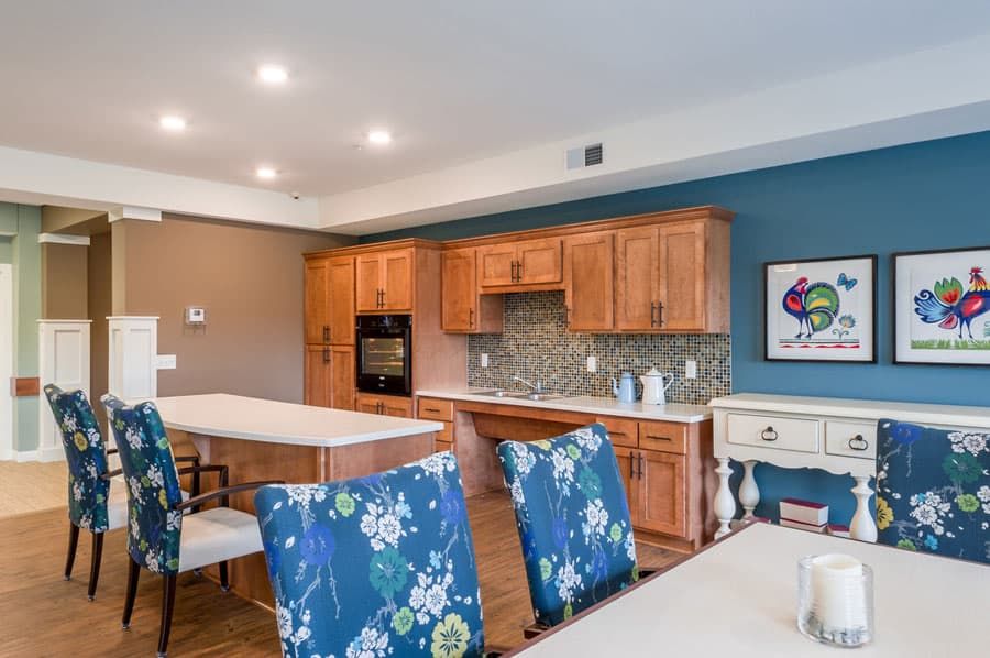 A modern kitchen and dining area featuring wooden cabinets and blue floral chairs.