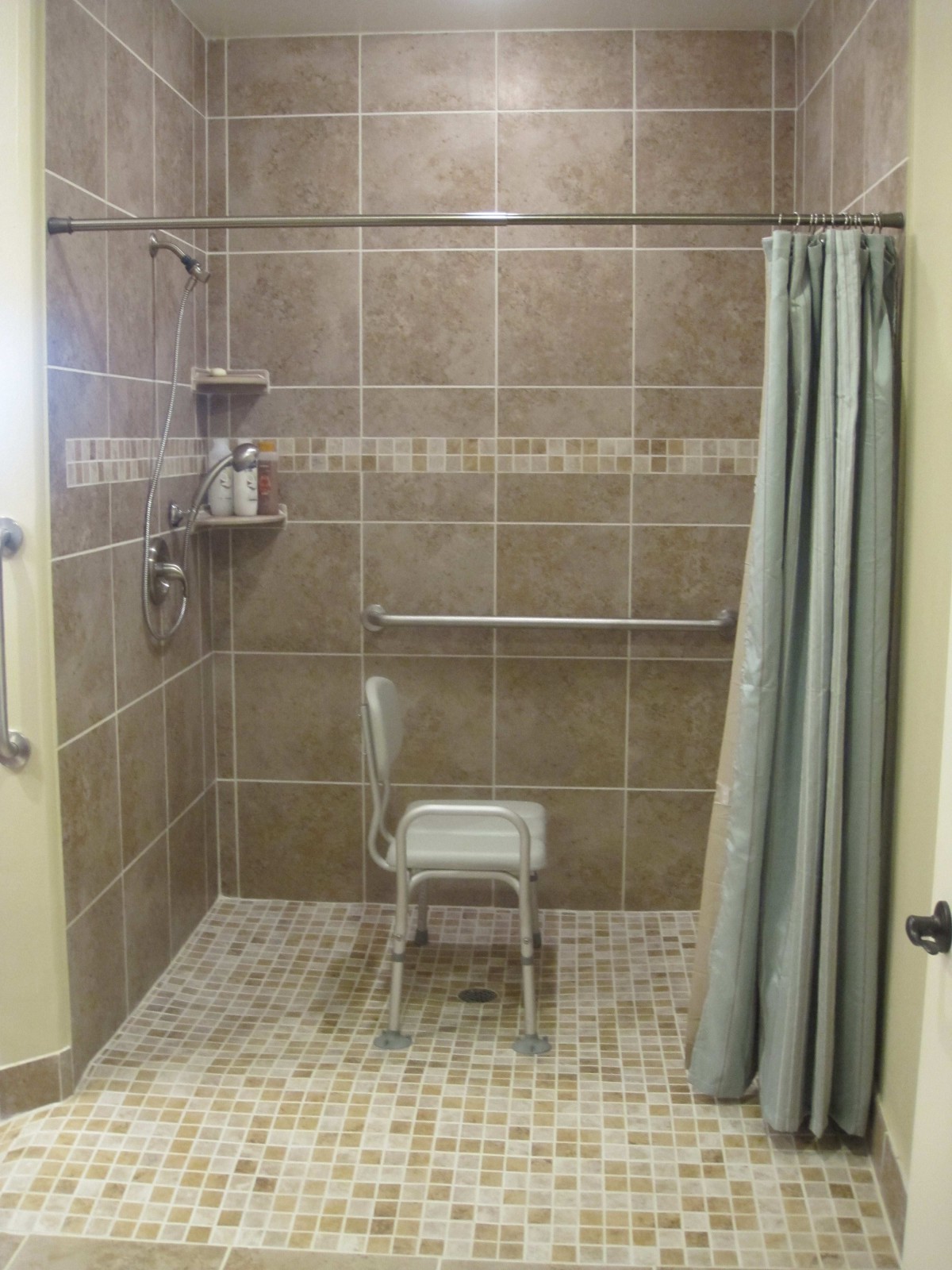 An accessible bathroom with a shower chair, grab bars, and tiled walls.