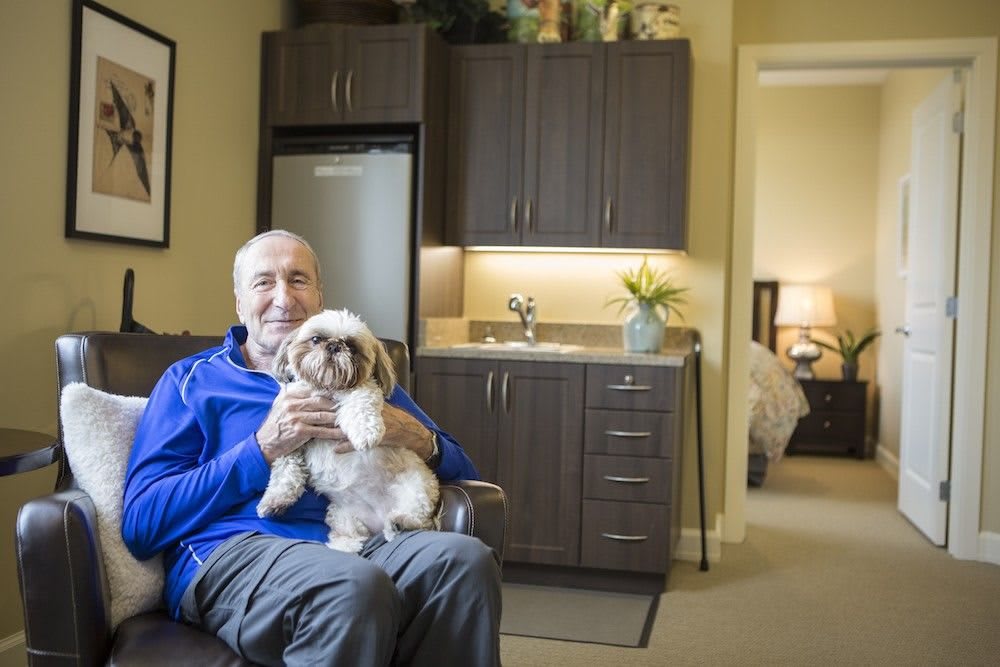 An elderly man sitting in a cozy living room, holding a small dog on his lap.