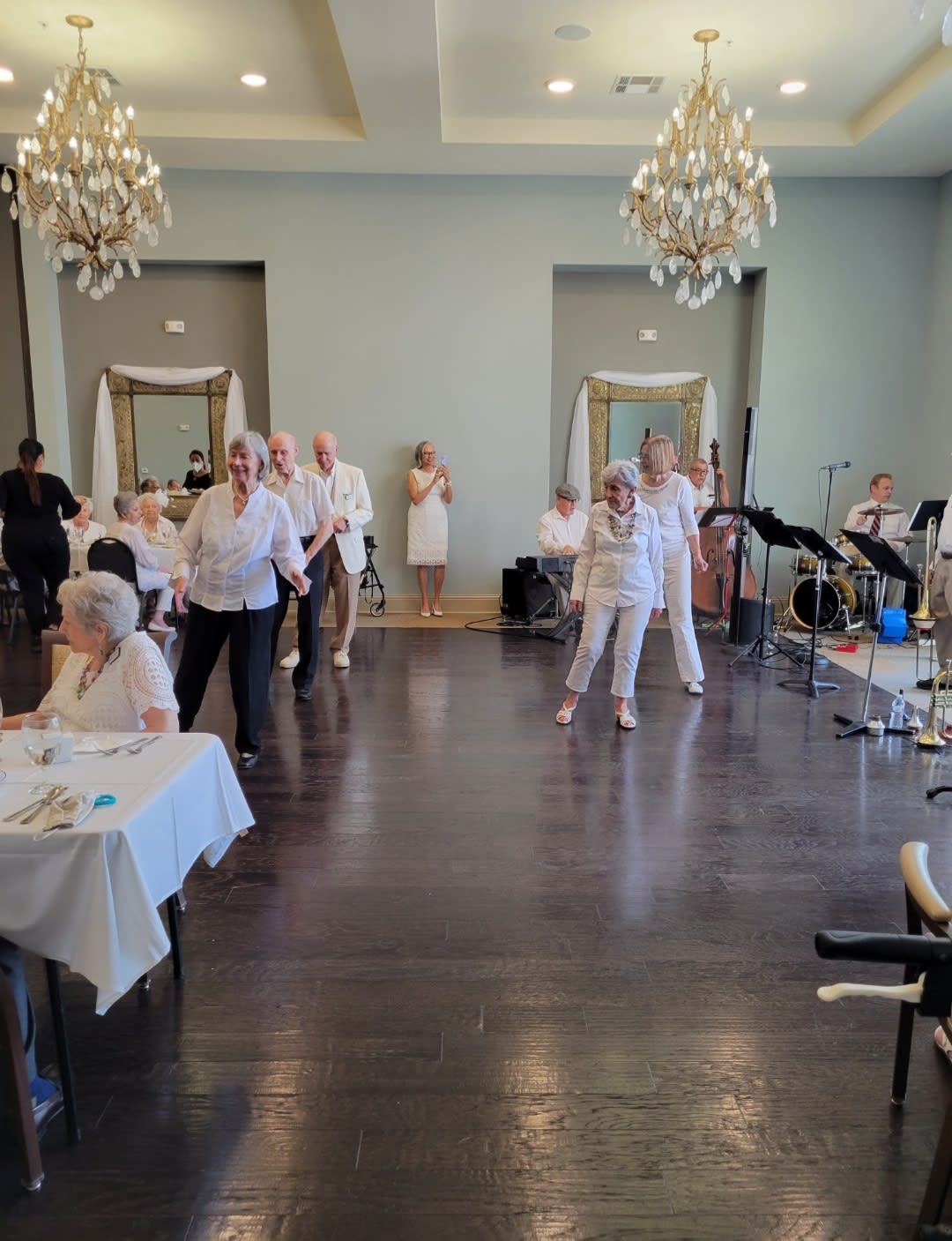 People enjoying a dance at an indoor event with elegant chandeliers.