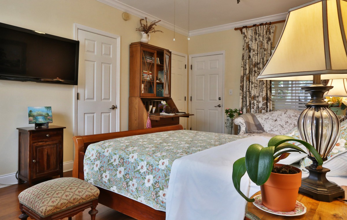A cozy bedroom interior featuring a wooden bed with floral bedding, a television mounted on the wall, and elegant decor.
