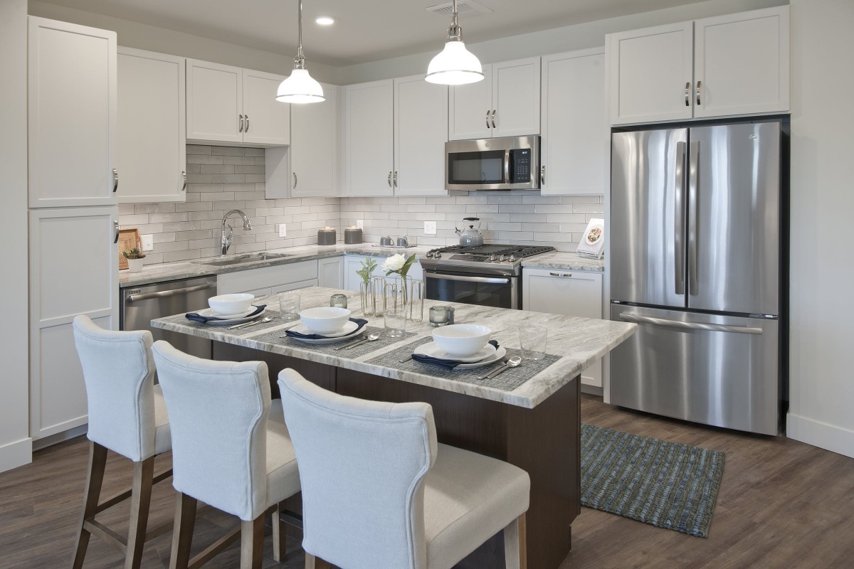 A modern kitchen with white cabinetry, stainless steel appliances, and a stylish kitchen island set for dining.