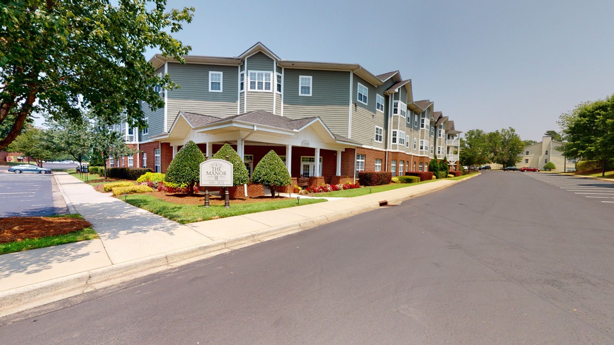A multi-story apartment building with well-maintained landscaping along a quiet street.