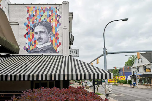 A vibrant mural of Nikola Tesla adorns the side of a building, showcasing street art in an urban setting.