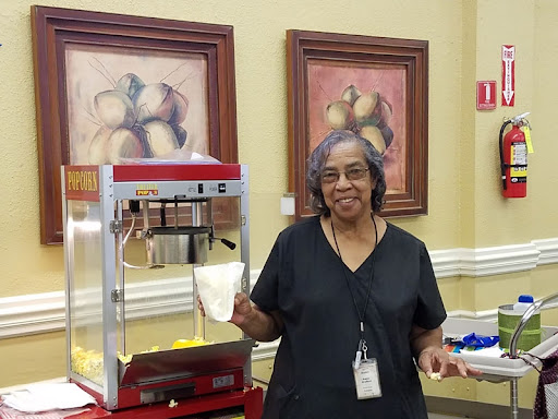 A woman stands beside a popcorn machine, ready to serve snacks at an indoor event.