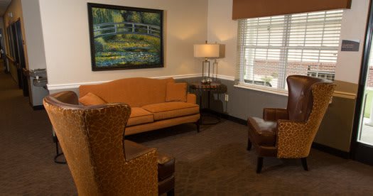A cozy living room with a warm color scheme, featuring a sofa, chairs, lamp, and a landscape painting on the wall.