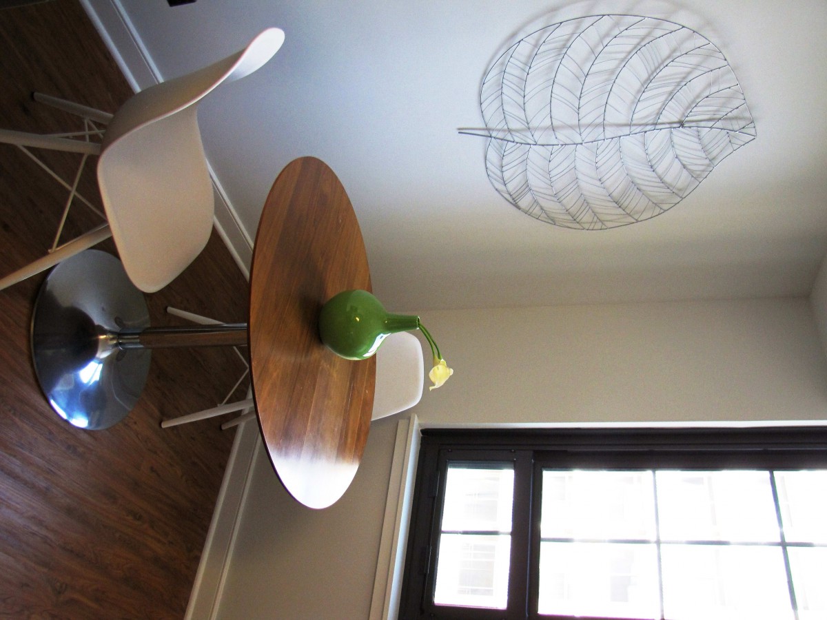 A modern dining area with a round wooden table, white chairs, and a vase with a flower.