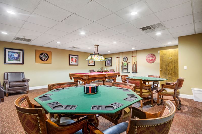 A recreational game room featuring a poker table, pool tables, and dart boards.