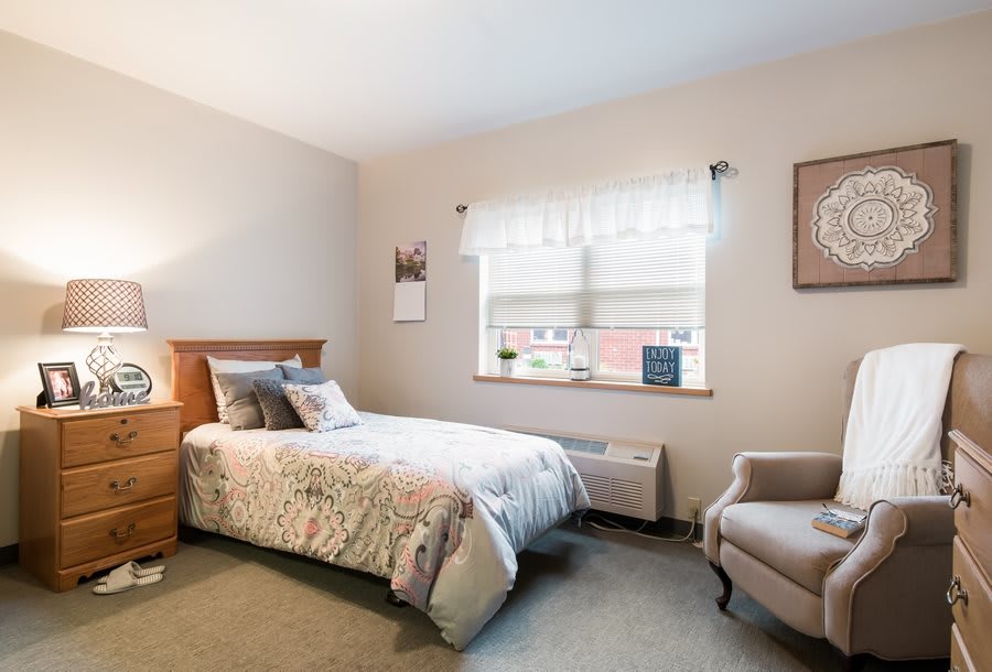 A cozy bedroom featuring a single bed with patterned bedding, an armchair, and a window allowing natural light to brighten the room.