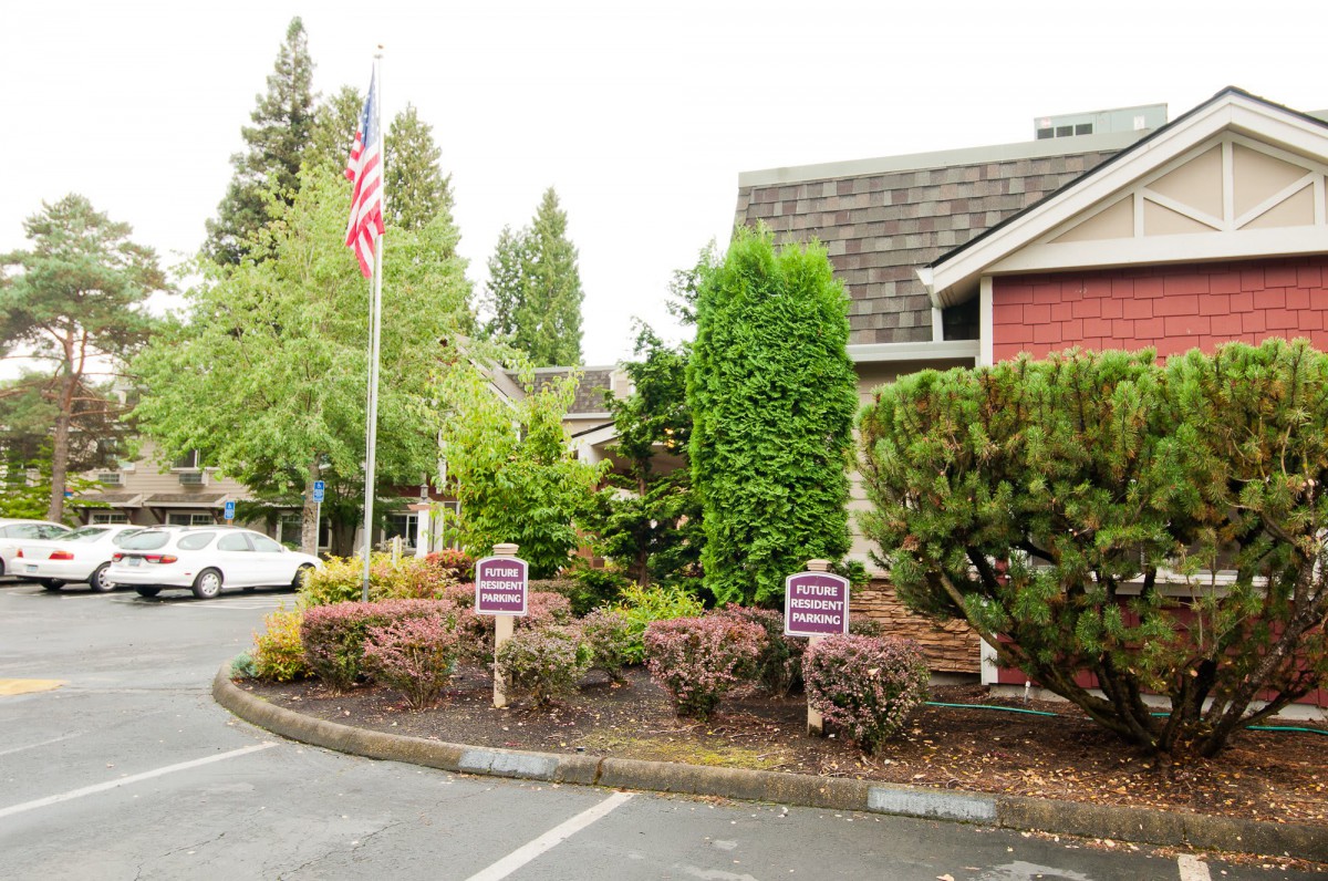A building with surrounding greenery and a parking lot that includes signs and an American flag.