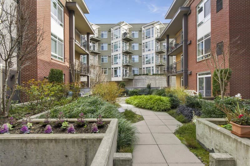 A modern apartment complex featuring a landscaped outdoor courtyard with a paved pathway.