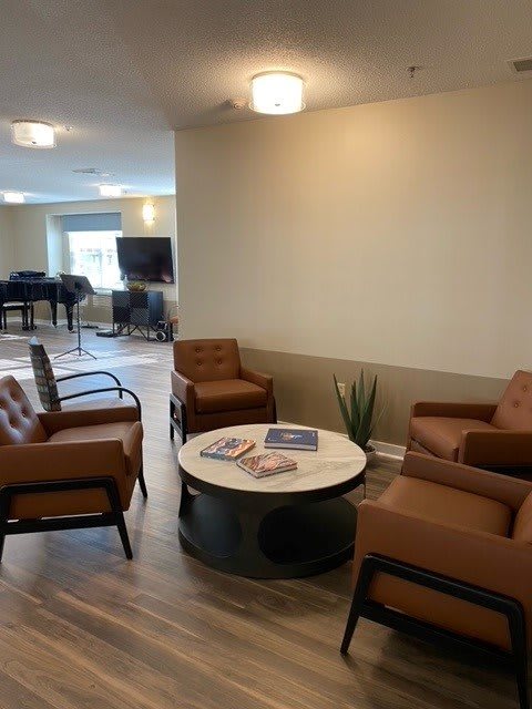 A modern living room with brown armchairs surrounding a coffee table, featuring a piano and television in the background.