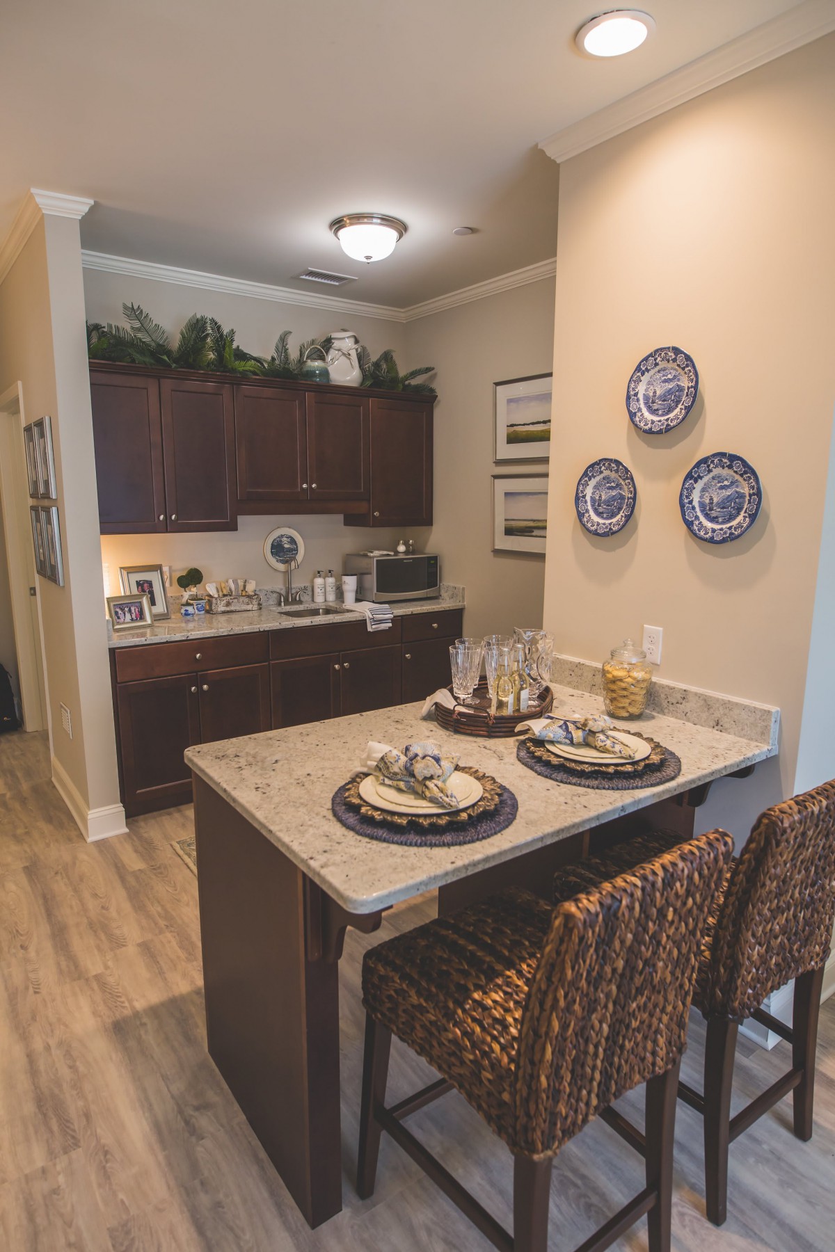 A cozy kitchen with a small dining area featuring bar stools and a countertop, adorned with decorative plates and set for two.