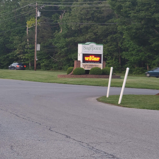 A roadside sign visible from a curve in the road, surrounded by greenery.