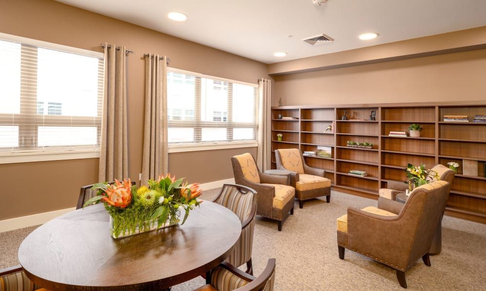 A cozy living room with comfortable chairs, a round table with a flower arrangement, and bookshelves along the wall.