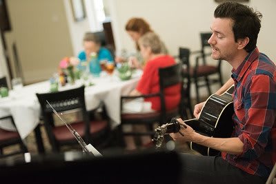 A guitarist performs for people dining indoors.