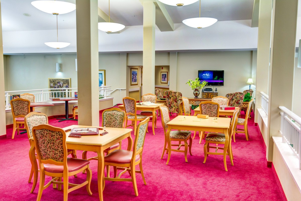A well-lit dining area with wooden tables and chairs on a red carpet.