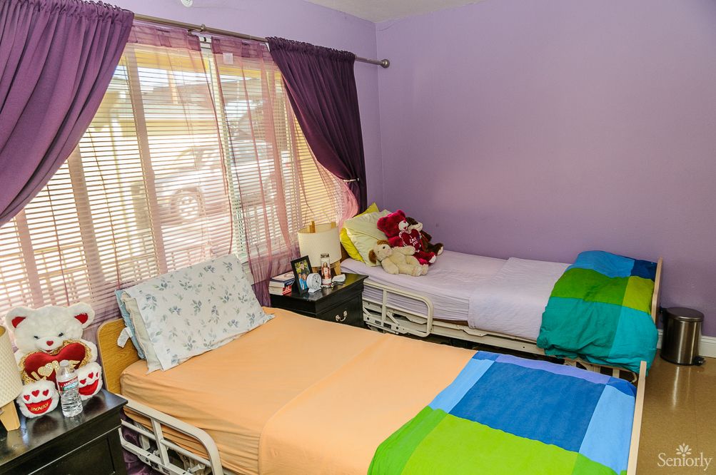 A cozy bedroom with two twin beds featuring colorful bedding, a window with purple curtains, and a nightstand in between.