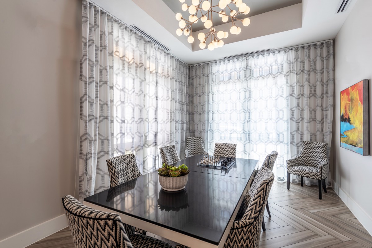 A modern dining room with a sleek black table, patterned chairs, and a striking chandelier.