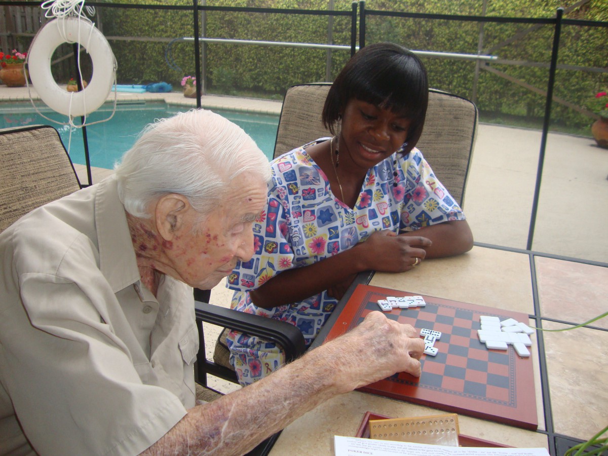 An elderly man playing checkers with a caregiver by the poolside.