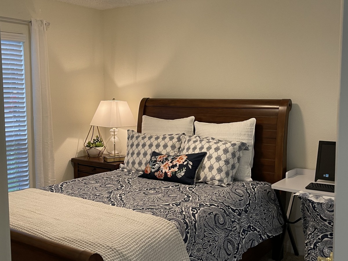 A cozy bedroom with a neatly made bed adorned with patterned pillows and a bedside lamp.