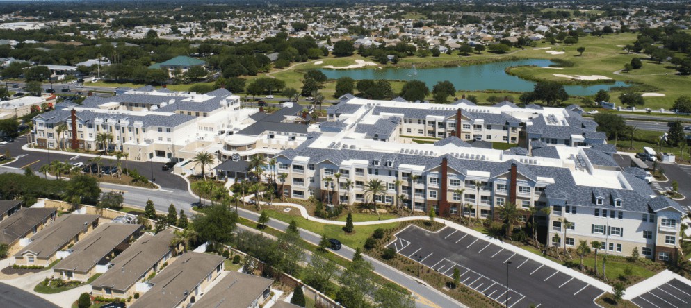 Aerial view of a modern apartment complex with surrounding greenery and a nearby lake.