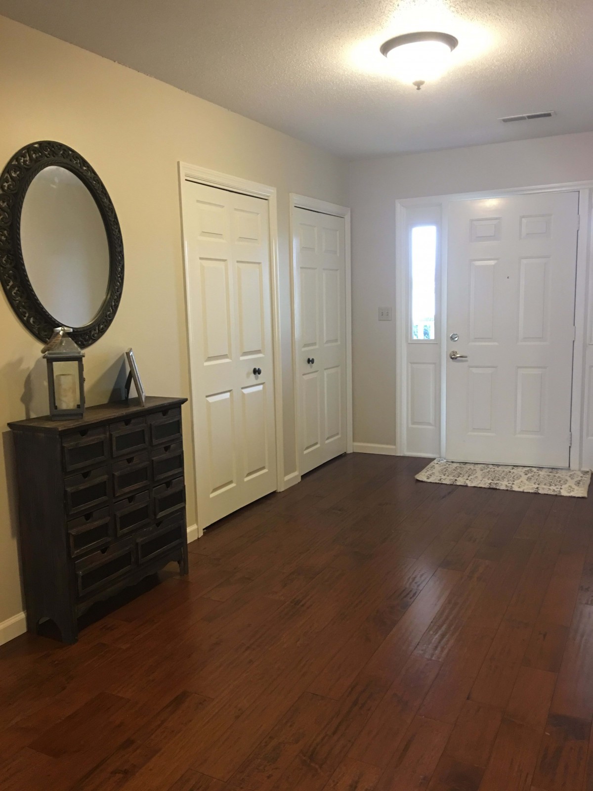 A neat entryway with a mirror above a dresser and a white front door.