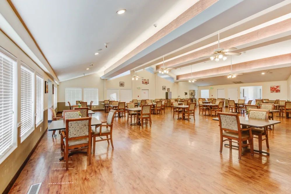 A spacious dining room with multiple tables and chairs, featuring wooden floors and ceiling lights.