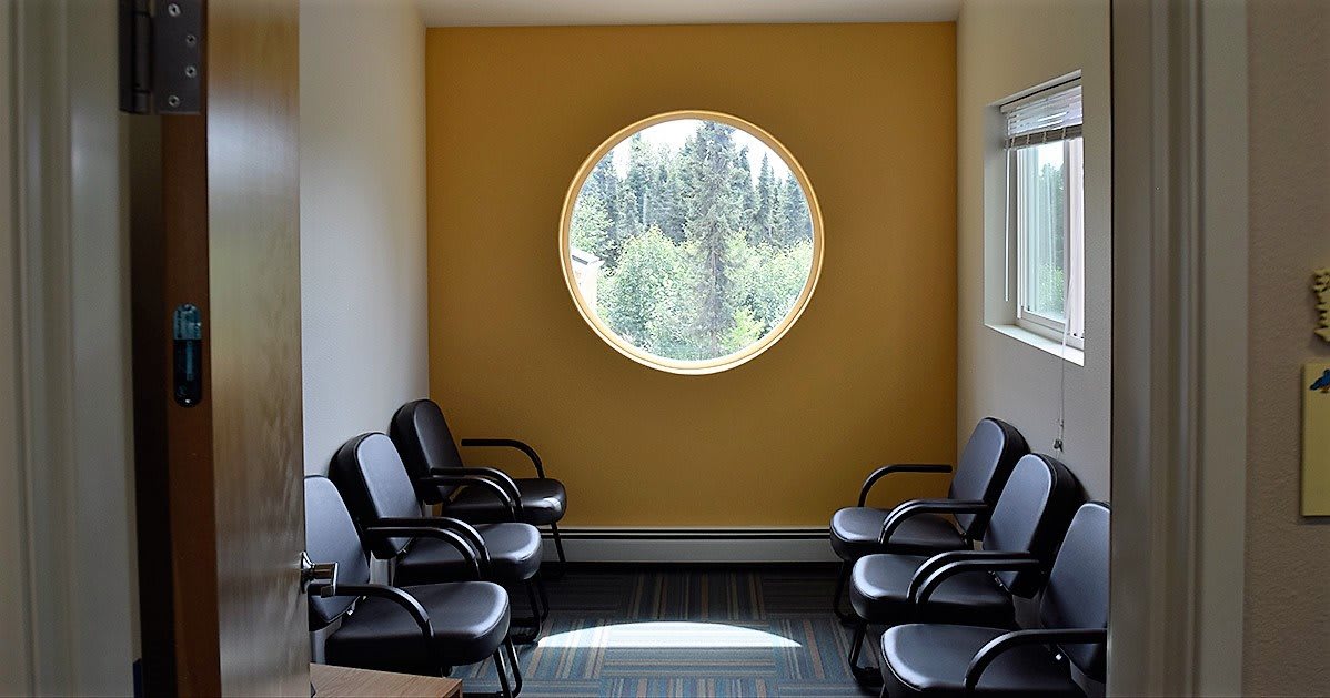 A modern waiting room with black chairs and a large circular window letting in natural light.