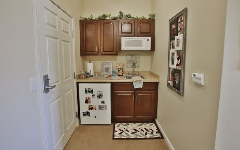 A cozy kitchenette with wooden cabinetry, a microwave, and a mini-fridge, adorned with decorative items.