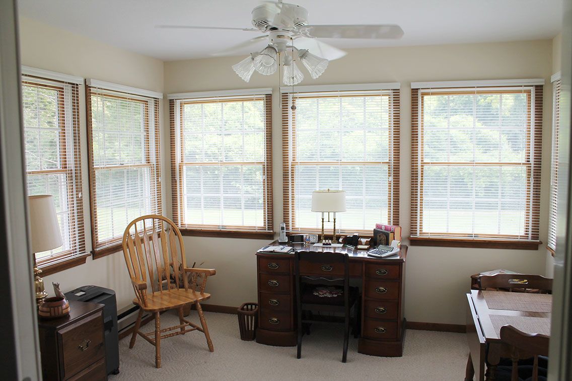 A cozy home office with a wooden desk, chair, and large windows providing natural light.