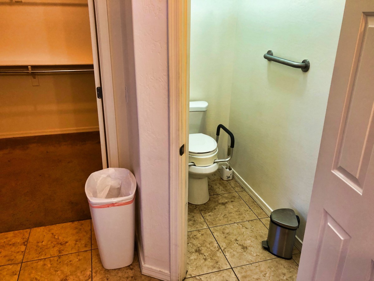 A view into a bathroom with a toilet and trash cans in a tiled setting.