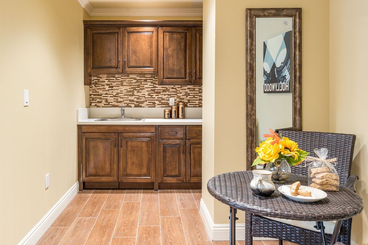 A cozy kitchen area featuring wooden cabinetry, a stone backsplash, and a small dining table with a floral centerpiece.