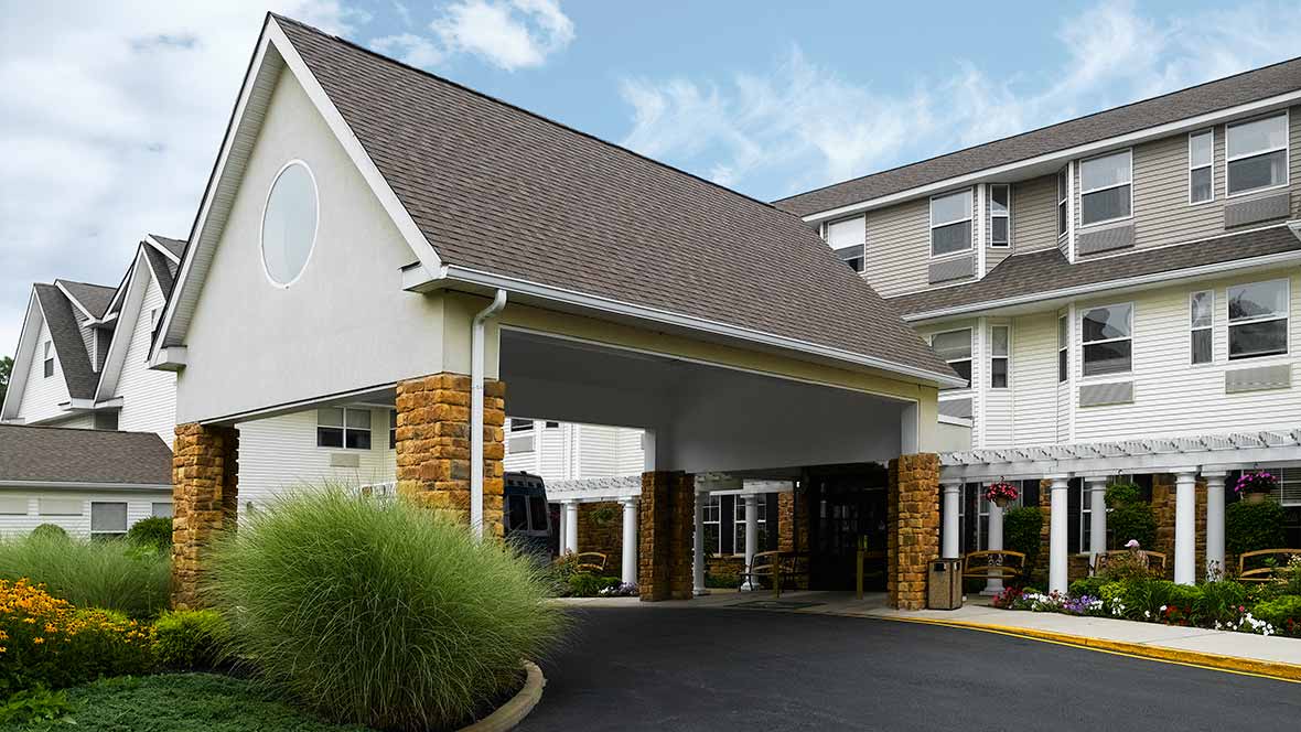 The image shows the entrance of a hotel with a modern design and landscaped surroundings.