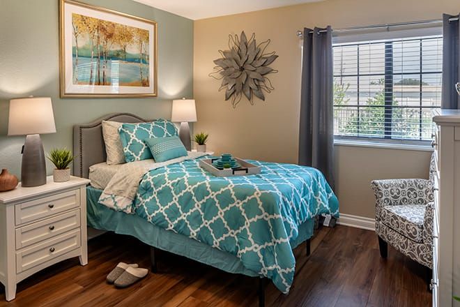 A cozy modern bedroom featuring teal bedding, elegant wall art, and wooden flooring.