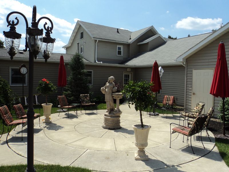 A cozy patio area with outdoor seating, statues, and umbrellas surrounded by a house.