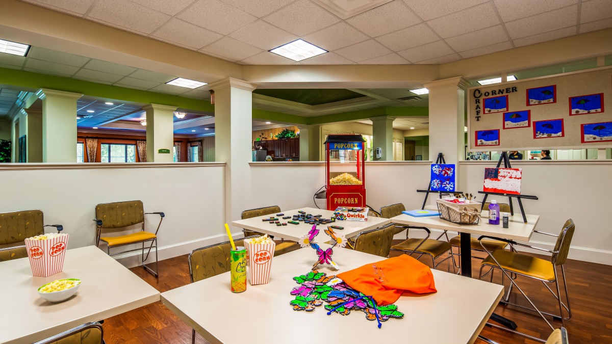 A spacious activity room featuring tables with craft supplies and a popcorn machine, set under bright indoor lighting.