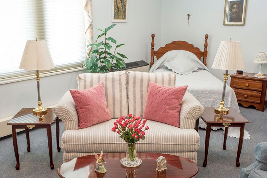 A cozy living space with a striped sofa and pink pillows, adjacent to a bed, featuring floral decor.