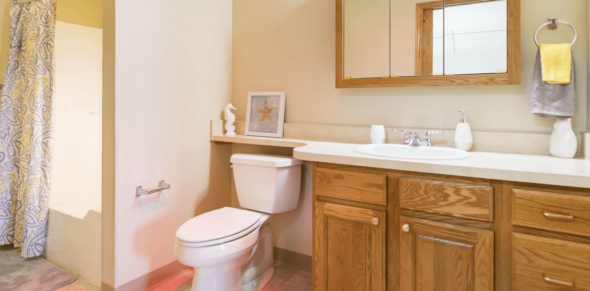 A neatly organized bathroom with a toilet and wooden cabinet sink.