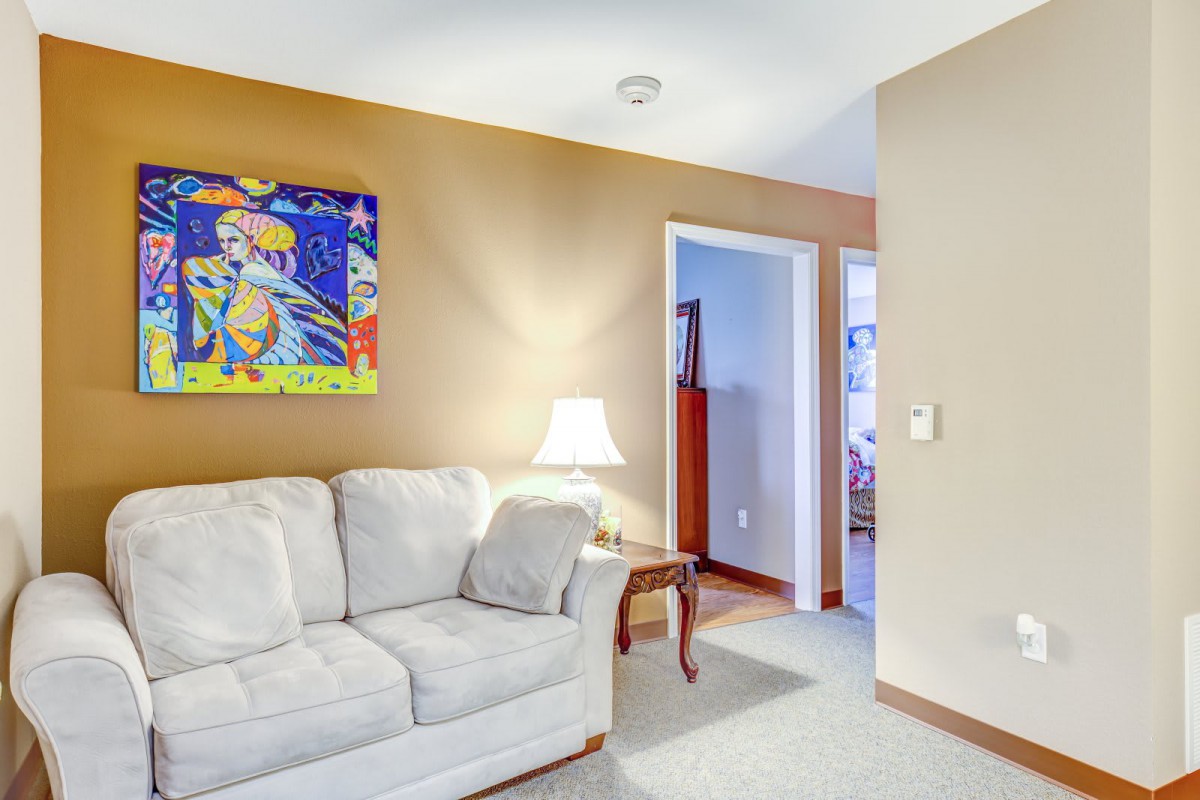 A cozy living room with a beige sofa, a lamp on a side table, and colorful wall art.