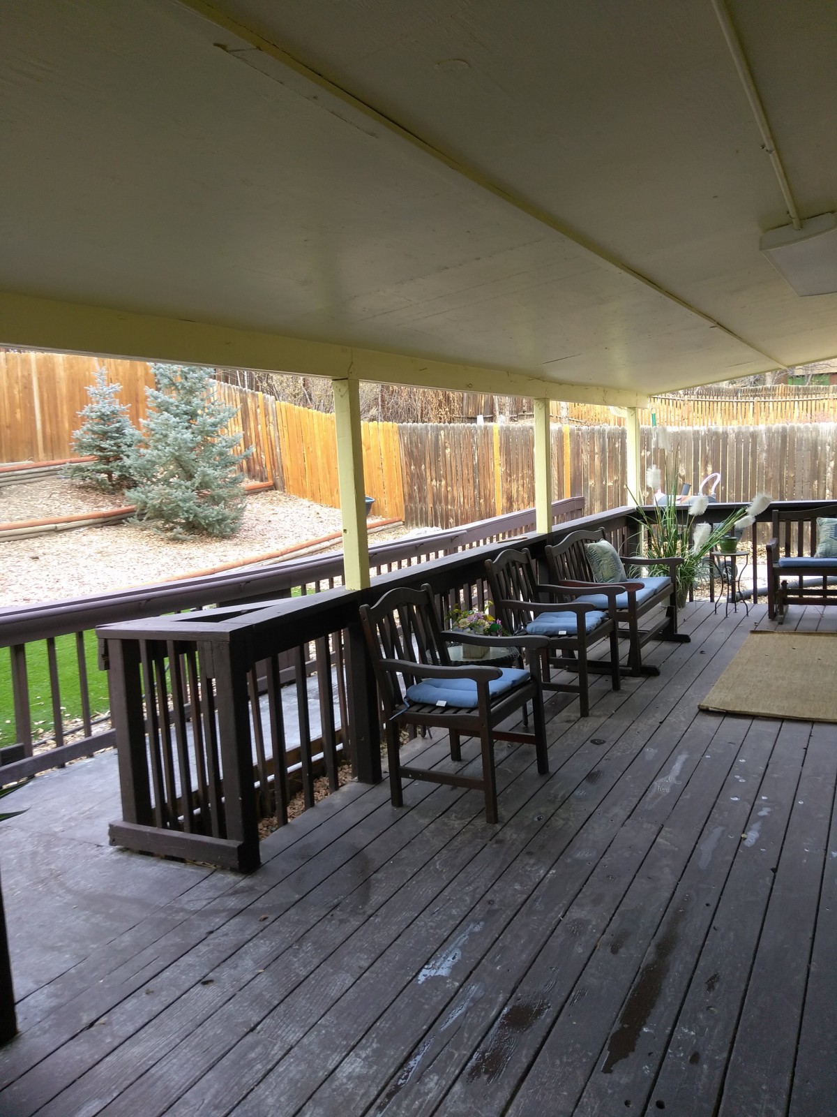 A spacious wooden deck with chairs overlooking a fenced backyard.