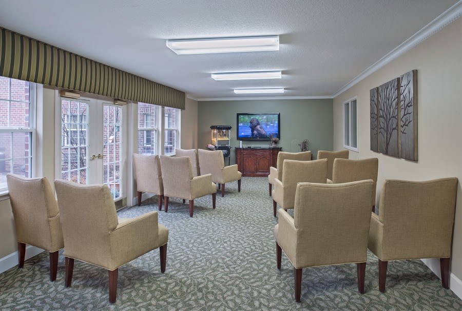 A cozy seating area with rows of comfortable chairs facing a television, set in a well-lit room.