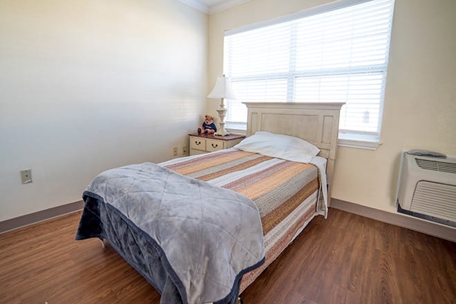 A cozy bedroom with a neatly made bed, a nightstand, and a large window.