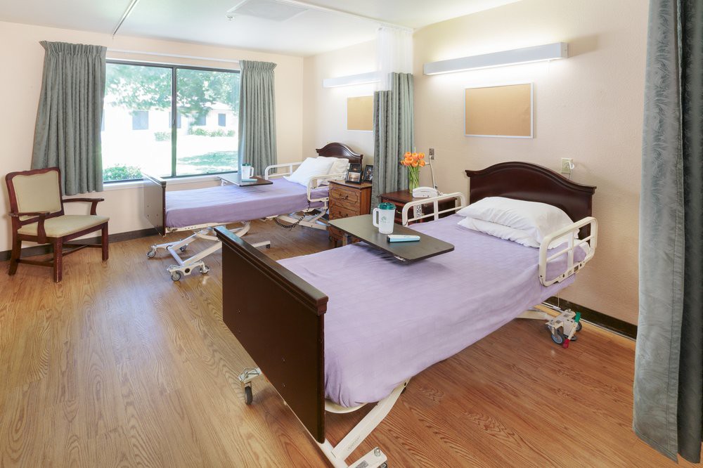 A clean and well-lit hospital room with two adjustable beds and a large window.